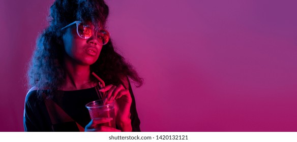Fashion young african girl black woman wear stylish pink glasses holding drink looking at camera isolated on party purple studio background, horizontal banner for website design, portrait, copy space