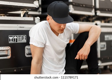 Fashion young man in a fashionable black cap with a stylish white t-shirt sitting near the boxes