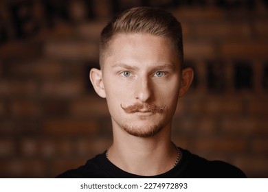 Fashion young man model with stylish hairdo, beard and 'handlebar' moustache looks confidently at camera on brick wall background. Barber fashion and beauty. Beauty hair salon, barbershop.