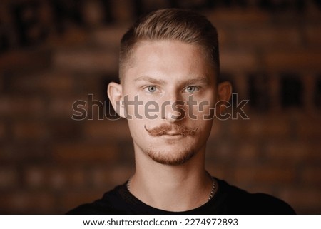 Fashion young man model with stylish hairdo, beard and 'handlebar' moustache looks confidently at camera on brick wall background. Barber fashion and beauty. Beauty hair salon, barbershop.