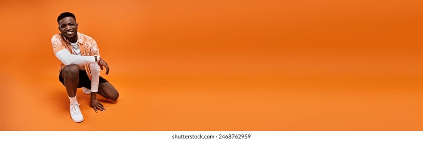 Fashionable African American man in stylish attire crouching on vibrant orange background. - Powered by Shutterstock