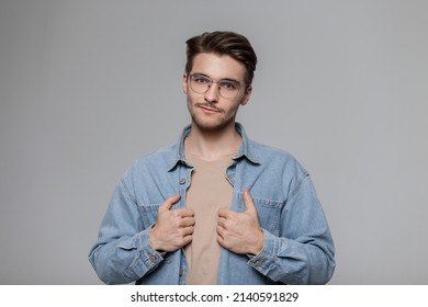 Fashionable American Hipster Man With Vintage Sunglasses, Denim Shirt And Beige T-shirt On A Gray Background In The Studio. Male Portrait 