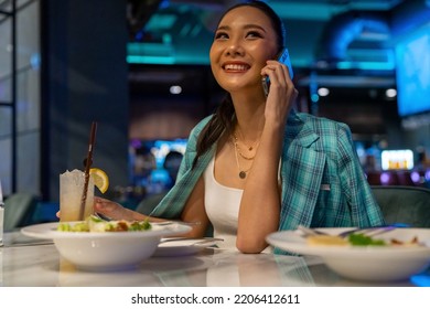 Fashionable Asian Woman Having Dinner And Talking On Mobile Phone At Luxury Restaurant Bar In The City At Night. Attractive Girl Enjoy And Fun Outdoor Lifestyle City Nightlife With Wireless Technology