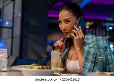 Fashionable Asian Woman Having Dinner And Talking On Mobile Phone At Luxury Restaurant Bar In The City At Night. Attractive Girl Enjoy And Fun Outdoor Lifestyle City Nightlife With Wireless Technology