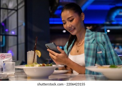 Fashionable Asian Woman Having Dinner And Using Mobile Phone At Luxury Restaurant Bar In The City At Night. Attractive Girl Enjoy And Fun Outdoor Lifestyle City Nightlife With Wireless Technology