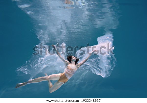 Fashionable and athletic girl free diver alone in\
the depths of the ocean. Swimmer brunette diving deep in ocean on\
blue underwater background. Pollution, plastic and ecology\
concept