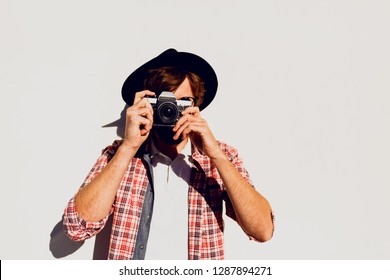 Fashionable  beard man portrait, using retro film camera, making  photos. Standing on white background. Hipster style. Wearing black hat, stylish eyeglasses, checkered shirt .