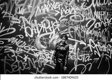 Fashionable beautiful african american woman posing in black leather jacket and pants at street against graffiti wall.