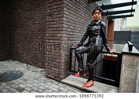 Fashionable beautiful african american woman posing in black leather jacket and pants at street.