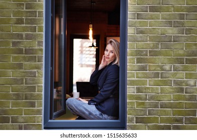 Fashionable beautiful businesswoman sitting in the window of the modern loft office. The model wears Stylish business clothes, black jacket, pants, accessories