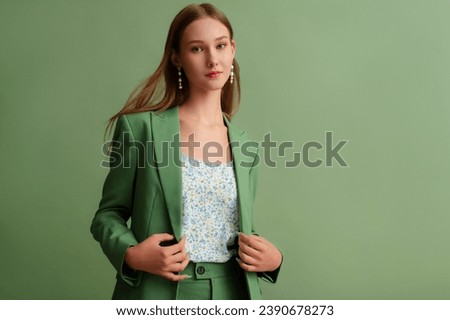 Fashionable beautiful confident woman wearing trendy suit blazer,  floral print top, pearl earrings, posing on green background. Copy, empty space for text