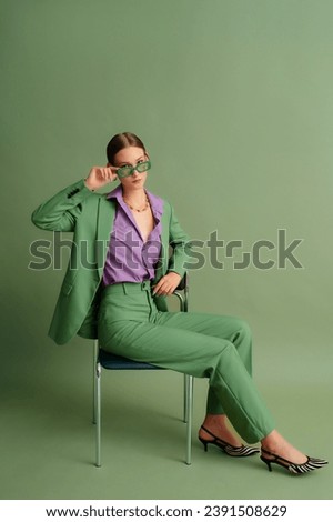  Fashionable beautiful confident woman wearing trendy color sunglasses, suit blazer, classic trousers, purple office shirt, zebra print pointed toe shoes, posing on green background