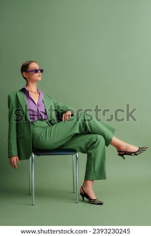  Fashionable beautiful confident woman wearing trendy color sunglasses, suit blazer, classic pants, purple office shirt, zebra print pointed toe shoes, posing on green background. Full-length portrait