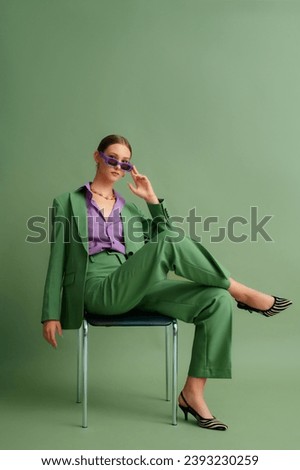  Fashionable beautiful confident woman wearing trendy color sunglasses, suit blazer, classic pants, purple office shirt, zebra print pointed toe shoes, posing on green background. Full-length portrait