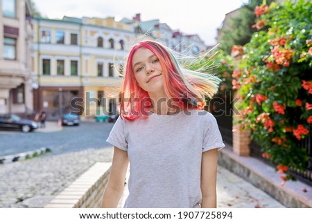 Fashionable beautiful girl teenager 16, 17 years old in wireless headphones with bright dyed colored hairstyle on the street of summer sunny city. Lifestyle, youth, fashion, beauty