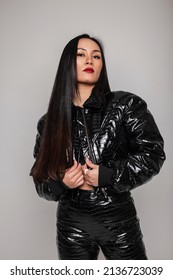 Fashionable Beautiful Young Asian Girl With Makeup And Long Hair In A Fashionable Black Snake Skin Outfit With A Jacket And Pants Poses In The Studio Against A Gray Background