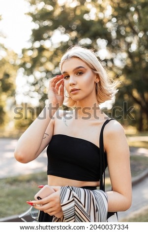 Fashionable beautiful young girl with short hair in fashionable clothes with tank top, shirt and cloth bag walking in the park