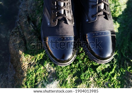 Fashionable black lace-up boots with patent toe on green grass background. Caucasus, Russia