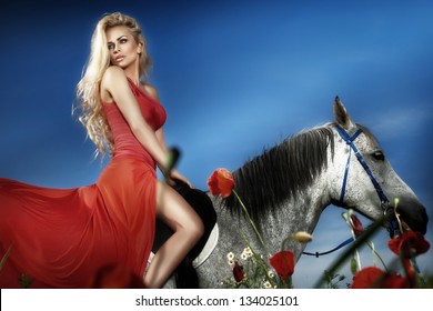 Fashionable blonde woman riding a horse in sunny day. Long curly hair.