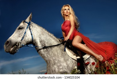 Fashionable blonde woman riding a horse in sunny day. Long curly hair.