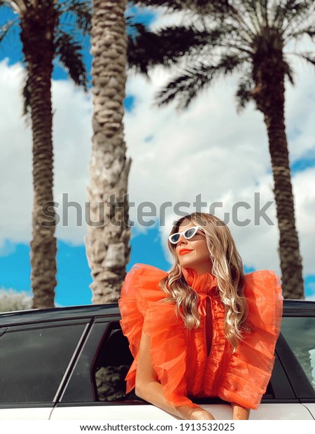 Fashionable blouse and posing through car\
window with palms trees in the\
background