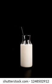 Fashionable bottle of milk on a total black background. Black straw in the bottle. The concept of a minimalist breakfast. Isolated on black