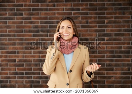 A fashionable businesswoman standing in front of a brick wall and talking on the phone. Business and telecommunications. A businesswoman using the phone.