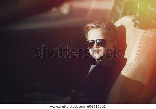 A fashionable child sits in the\
car in the summer. Trendy boy in sunglasses inside the\
car