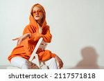 Fashionable confident blonde woman wearing trendy orange sweatshirt, color sunglasses, posing on white background. Copy, empty space for text