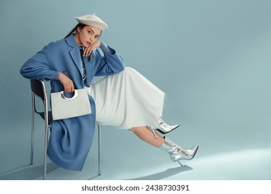 Fashionable confident woman wearing beret, elegant blue coat, white denim maxi skirt, silver ankle boots, holding stylish faux leather purse, posing on blue background. Full-length studio portrait - Powered by Shutterstock