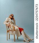 Fashionable confident woman wearing elegant white woolen coat, sunglasses, high leather heeled boots, posing on blue background. Full-length studio fashion portrait. Copy, empty space for text
