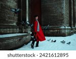 Fashionable confident woman wearing elegant long red coat, cap, knitted scarf, walking in street of European city. Full-length outdoor fashion portrait. Copy, empty, blank space for text