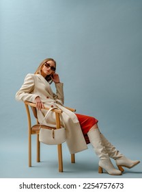 Fashionable confident woman wearing elegant white woolen coat, sunglasses, high leather heeled boots, posing on blue background. Full-length studio fashion portrait. Copy, empty space for text - Shutterstock ID 2254757673