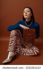 Fashionable confident woman wearing stylish blue turtleneck, trendy flared trousers with zebra print, white cowboy boots, holding brown suede fringed bag. Studio portrait  - Shutterstock ID 2252351213