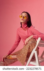 Fashionable confident woman wearing trendy yellow sunglasses, pink turtleneck top, sequined flare trousers, golden pointed toe shoes - Shutterstock ID 2232278571