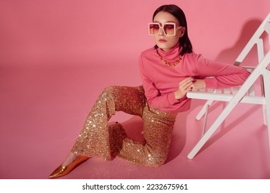 Fashionable confident woman wearing trendy 70s style outfit with big sunglasses, pink turtleneck top, sequined flare trousers, golden  shoes. Full-length studio portrait. Copy, empty space for text - Shutterstock ID 2232675961