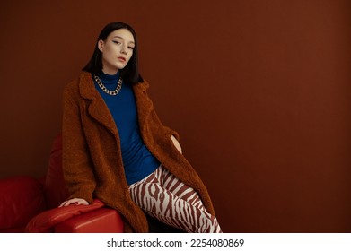 Fashionable confident woman wearing trendy blue turtleneck, brown faux fur coat, chunky chain, trousers with zebra print. Studio fashion portrait. Copy, empty space for text - Shutterstock ID 2254080869