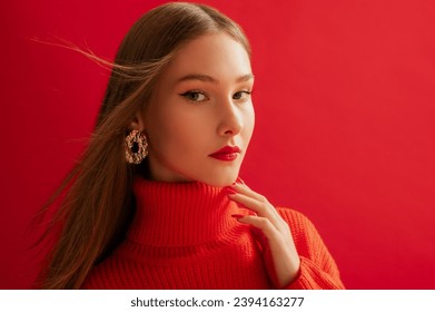 Fashionable confident woman wearing trendy big golden earrings, red knitted turtleneck sweater dress, posing on red background. Close up studio fashion portrait. Copy, empty space for text - Shutterstock ID 2394163277