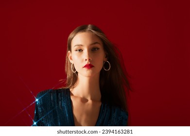 Fashionable confident woman wearing trendy rhinestone hoop earrings, blue sequin dress, posing on red background. Close up studio fashion portrait. Copy, empty space for text - Shutterstock ID 2394163281