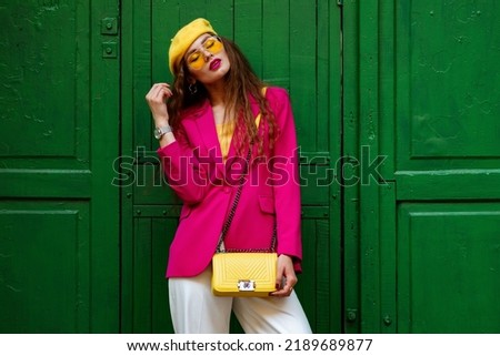 Fashionable confident woman wearing trendy outfit with yellow sunglasses, beret, wrist watch, shoulder bag, pink fuchsia color blazer, posing near green door. Copy, empty space for text