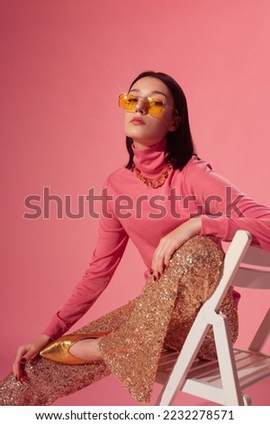 Fashionable confident woman wearing trendy yellow sunglasses, pink turtleneck top, sequined flare trousers, golden pointed toe shoes