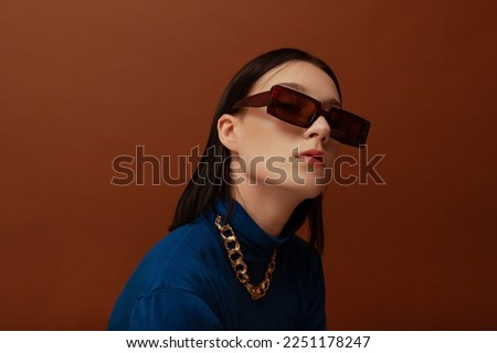 Fashionable confident woman wearing trendy brown rectangular sunglasses, chunky chain, stylish blue turtleneck. Close up studio portrait. Copy, empty space for text