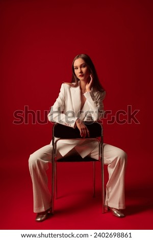 Fashionable confident woman wearing trendy white suit double breasted blazer, classic trousers, metallic color shoes, posing on red background

