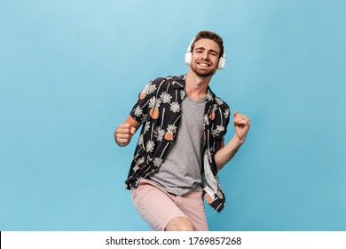 Fashionable Cool Man With Beard In Grey T-shirt, Pineapple And Palm Print Shirt And Shorts Smiling, Looking Into Camera And Posing With Headphones..