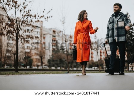 A fashionable couple strolls along an urban street carrying luggage, implying a casual city break or weekend getaway vibe.