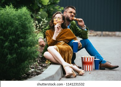 Fashionable Couple In Velvet Clothing Eating Fried Chicken Legs On Street