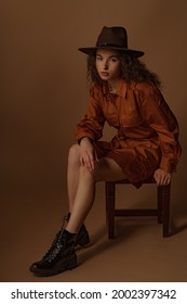 Fashionable Curly Brunette Woman Wearing Brown Cotton Mini Shirt Dress, Trendy Track Sole Leather Boots, Posing In Studio. Full-length Studio Portrait