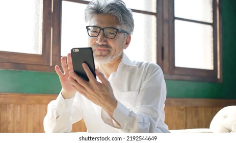 Fashionable Elderly Asian Man Using A Smart Phone In The Room.