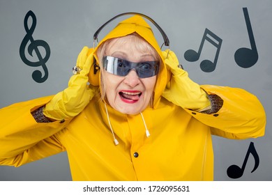 A fashionable elderly lady in yellow is listening to music with headphones. The concept of a party, a disco, a young state of mind. Close-up on a gray background. - Shutterstock ID 1726095631