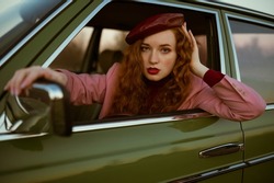 Fashionable Elegant Confident Redhead Woman With Marsala Color Lips, Eyes Makeup, Wearing Faux Leather Beret, Classic Pink Blazer, Posing, Sitting In The Green Vintage Car